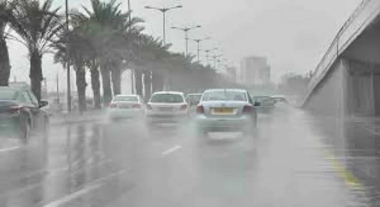 Voitures sous une pluie intense sur une route urbaine en Algérie.