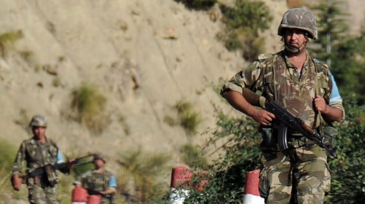 Soldat en uniforme militaire avec arme dans un paysage rocheux.