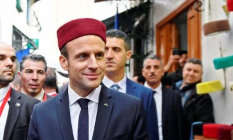 Emmanuel Macron lors d'une visite officielle en Algérie, entouré de plusieurs personnes.