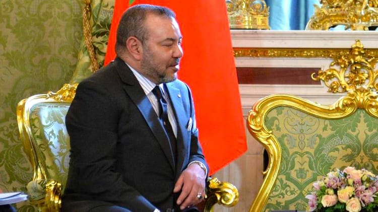 Homme politique en réunion officielle avec décor luxueux et drapeau marocain en arrière-plan.