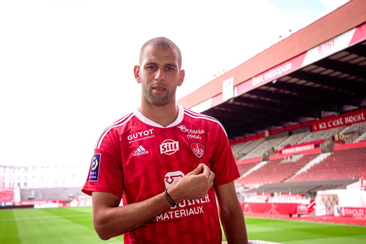 Slimani en maillot de football rouge dans un stade vide.