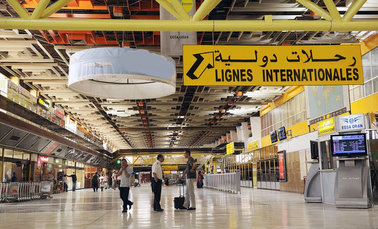 Hall d'arrivée international à l'aéroport d'Oran avec panneaux en français et arabe.