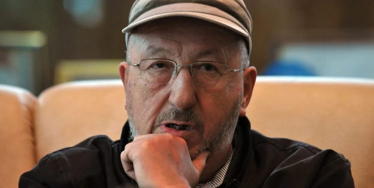 Homme âgé portant une casquette et des lunettes, en pleine réflexion.