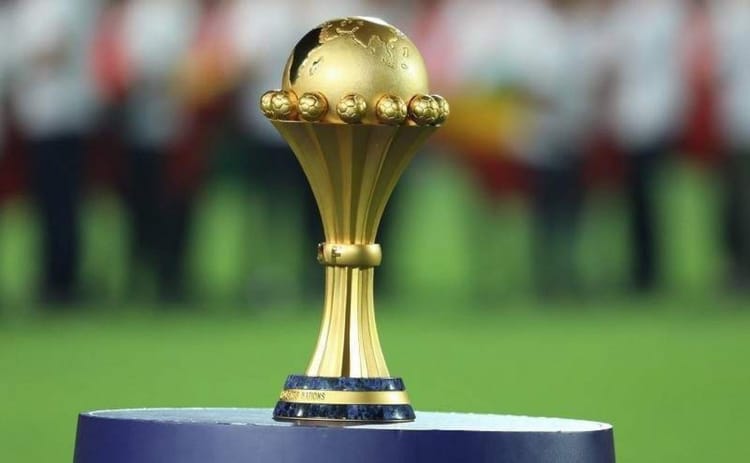 Trophée de la CAN 2025 sur un podium avec public en arrière-plan.