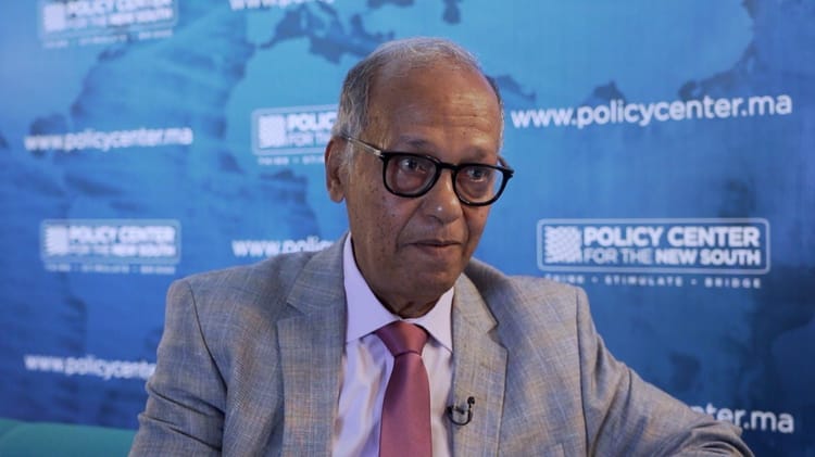 Abdelhak Bassou en discussion, portant un costume et des lunettes.