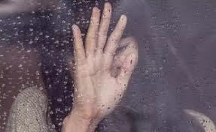 Femme derrière une vitre, main levée, sous la pluie.