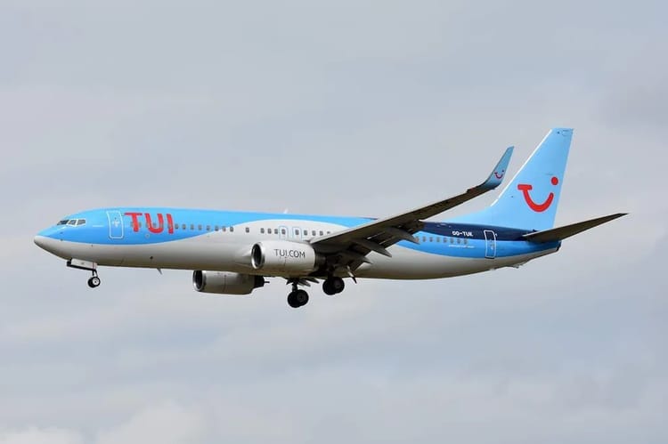 Avion TUI Fly bleu en vol dans le ciel nuageux.