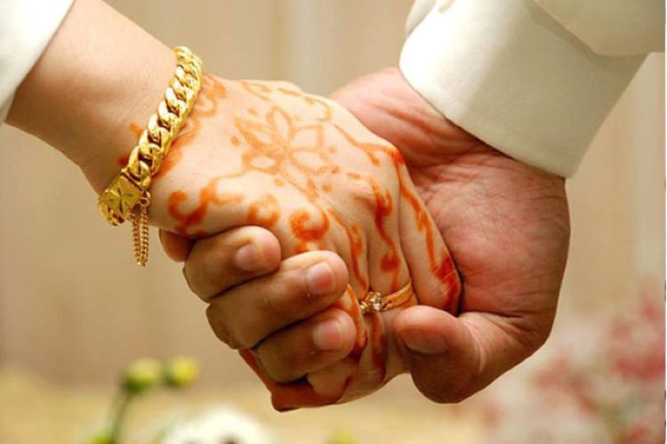 Main d'une femme avec henna et bijoux tenant la main d'un homme.