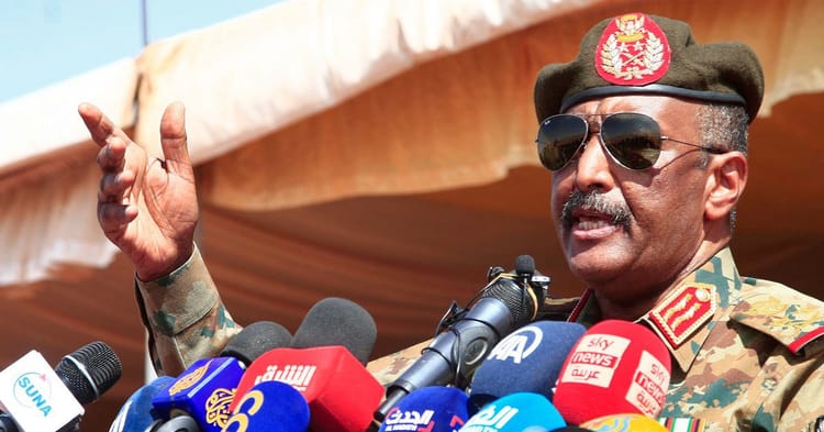 Officier militaire soudanais parlant lors d'une conférence avec microphones.