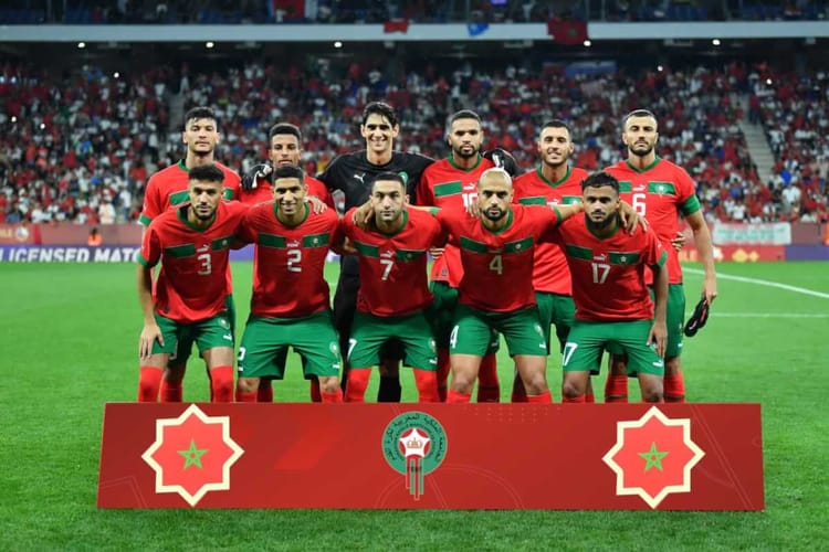 Groupe de joueurs marocains en tenue rouge et verte sur le terrain de football.
