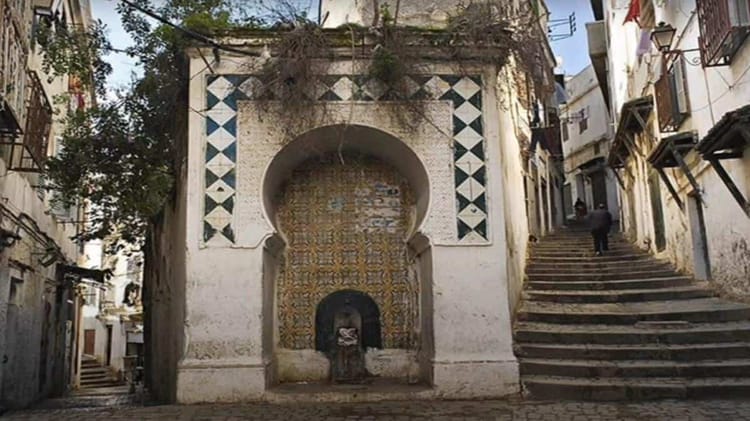 Fresque murale en Algérie avec motifs géométriques et fontaine ancienne.