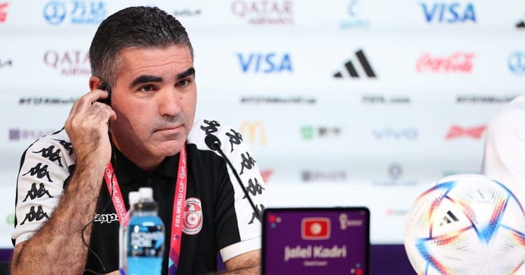 Homme en conférence de presse, portant maillot de football, parlant à un micro.