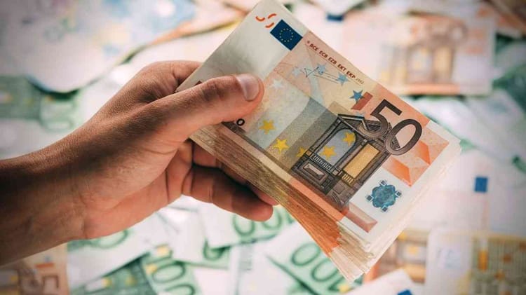 Main tenant des billets de 50 euros avec d'autres billets en arrière-plan.