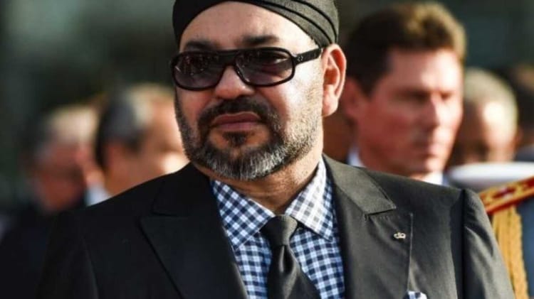 Homme en costume noir et lunettes de soleil lors d'un événement public.