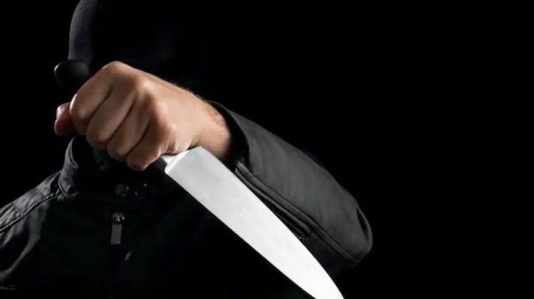 Homme masqué tenant un couteau dans une main dans l'obscurité.