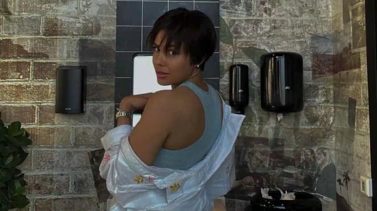 Caroline Chahinez pose dans un lieu public avec mur en briques.