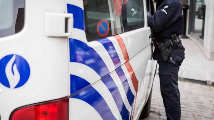 Agent de police belge en action devant un véhicule de police.