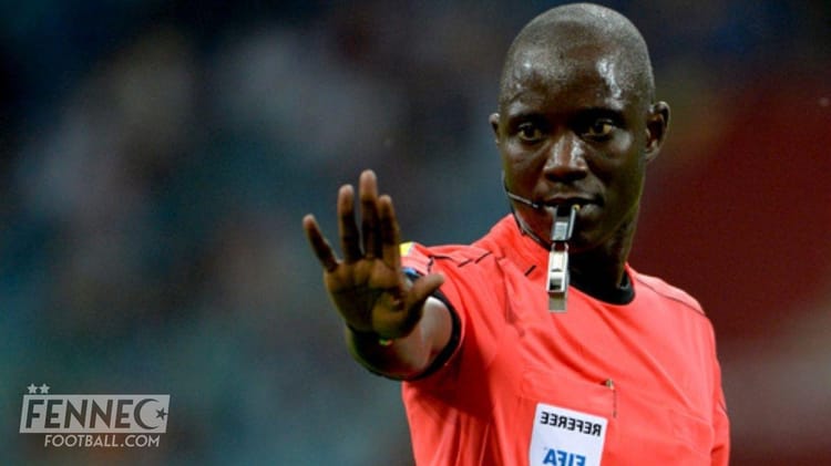 Arbitre Gassama avec sifflet, signalant une faute lors d'un match de football.