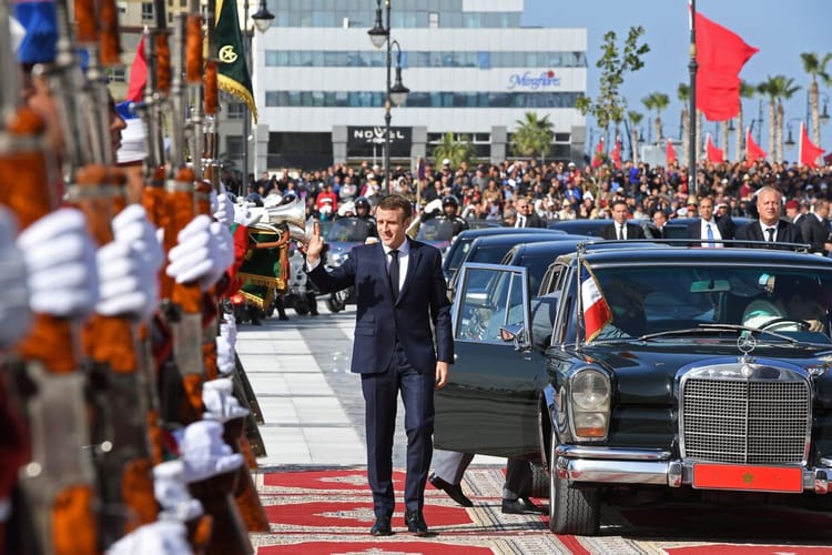 Personne en costume officiel saluant lors d'une cérémonie publique en plein air.