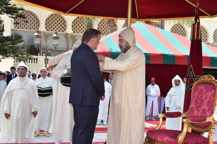 Homme en costume et homme en tenue traditionnelle lors d'une cérémonie.