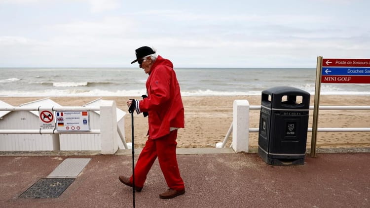 Homme en manteau rouge et chapeau sur la promenade de plage.
