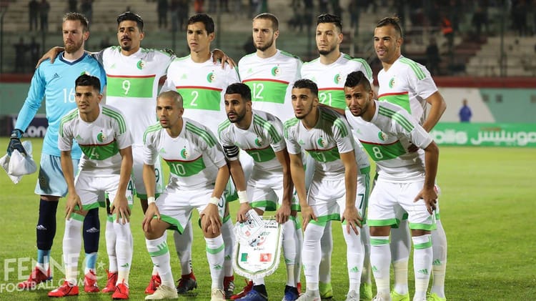 Groupe de joueurs de football algériens en tenue officielle sur le terrain.