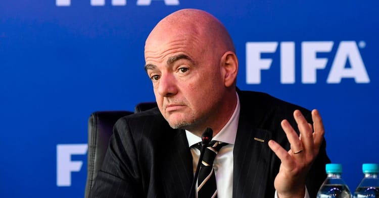 Homme en costume lors d'une conférence FIFA, expression perplexe.