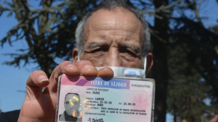 Homme âgé tenant une carte d'identité, visage sérieux, arrière-plan naturel.