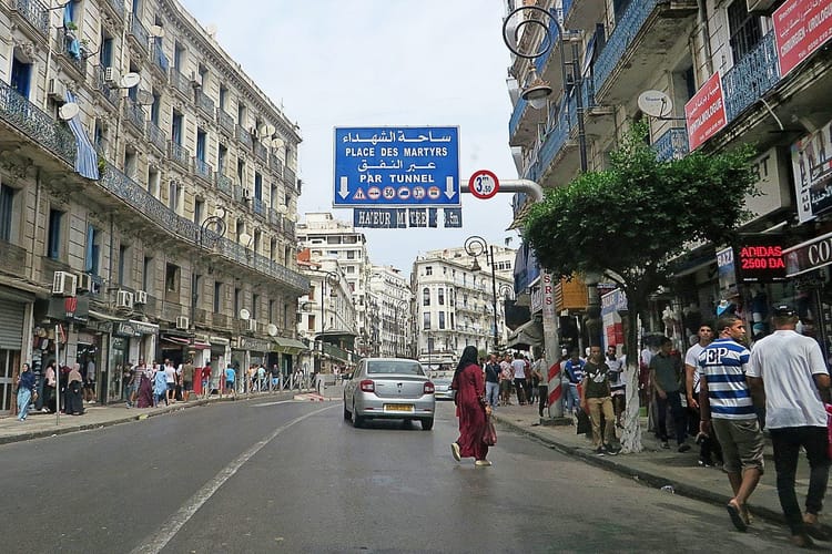 Rue animée à Alger avec des passants et des voitures.