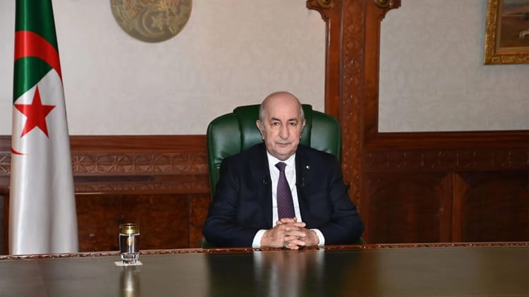 Président Tebboune assis à son bureau avec drapeau algérien en arrière-plan.
