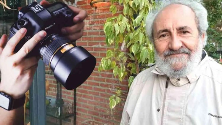 Homme âgé avec barbe blanche, souriant, en extérieur avec végétation.