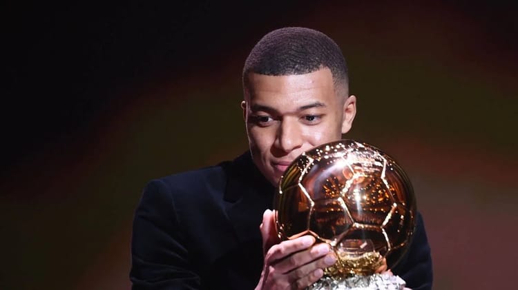 Kylian Mbappé tenant le Ballon d'Or 2023, souriant.
