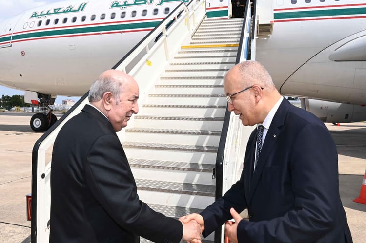 Tebboune et un officiel se serrent la main à l'aéroport.