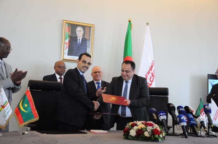 Hommes d'affaires signant un document officiel avec drapeaux algérien et d'autres pays.