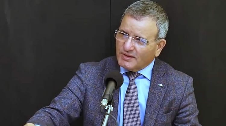 Ali Ghediri en conférence, portant costume et lunettes.
