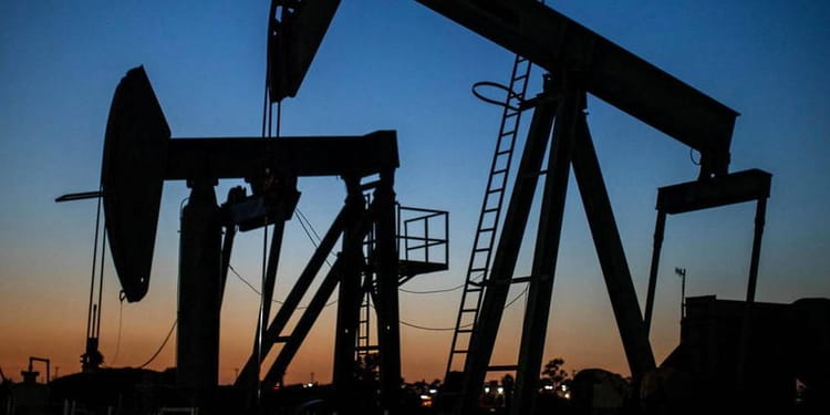 Puits de pétrole en activité au coucher du soleil, silhouette sombre contre ciel coloré.