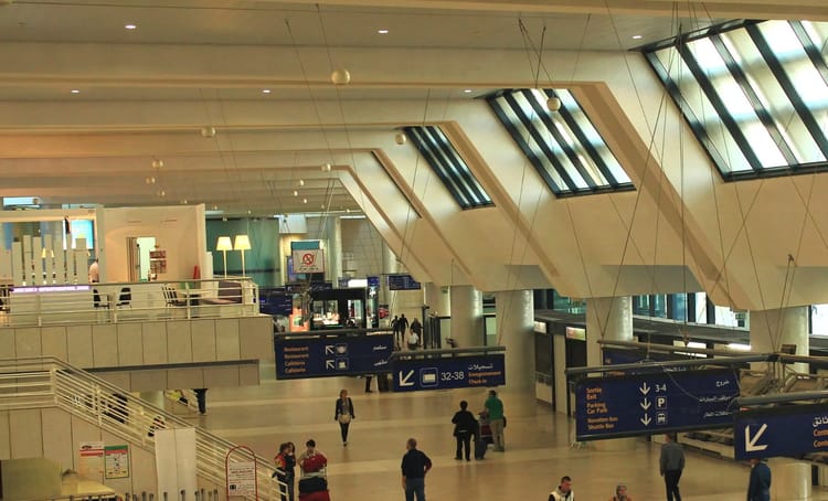 Message d'une cliente destiné à l'aéroport d'Alger : « Même mon chat n’aurait pas accepté » Vue intérieure de l'aéroport d'Alger avec passagers et panneaux d'orientation.