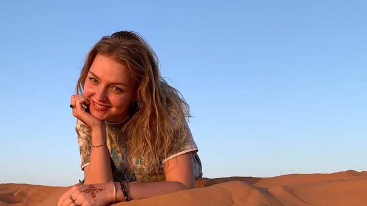 Cette algérienne de France tombe d’admiration pour l’Algérie à cause de ceci… Jeune femme souriante dans le désert, paysage ensoleillé et ciel bleu clair.
