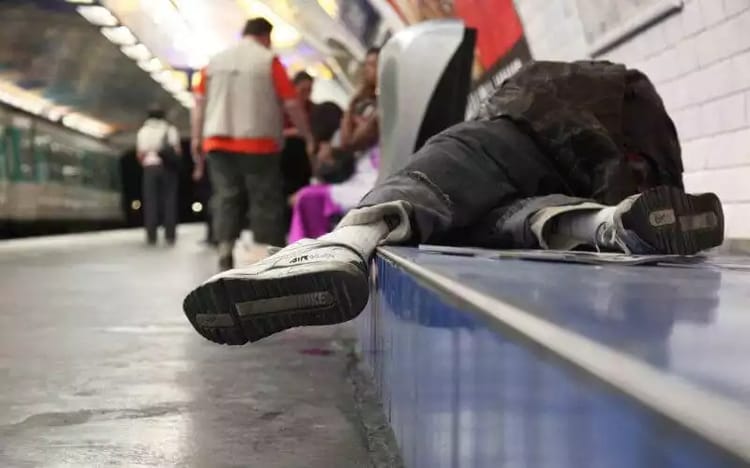 Homme sans-abri allongé sur le sol d'une station de métro.