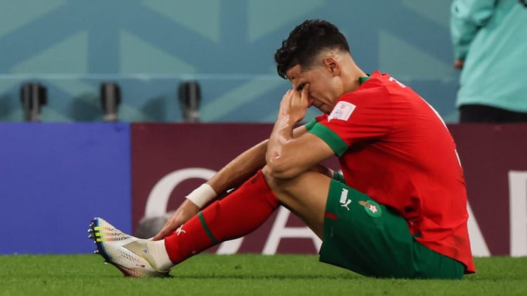Joueur marocain assis par terre, visiblement déçu, lors d'un match de football.