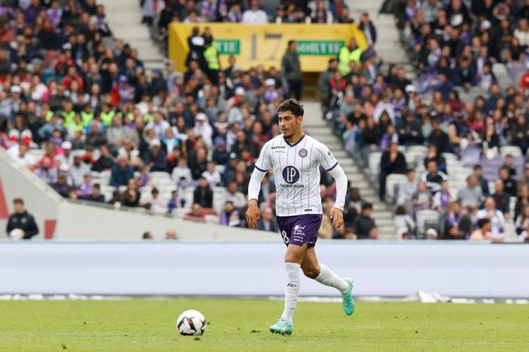 Farès Chaïbi joue au football sur le terrain avec un public en arrière-plan.