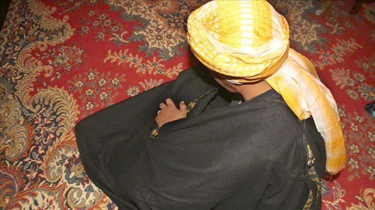 Homme portant un turban algérien traditionnel sur un tapis coloré.
