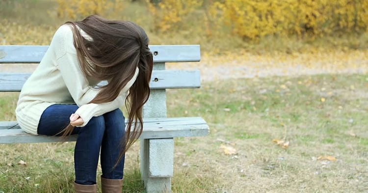 Jeune femme triste assise sur un banc dans un parc.