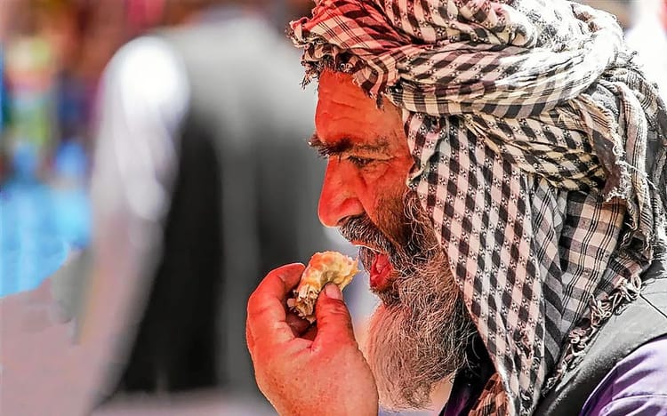FAO : la population mondiale ménacée par la faim, l'Afrique plus touchée Homme avec turban mangeant dans un marché africain animé.
