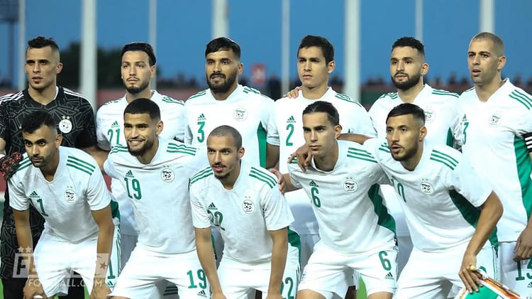 Groupe de joueurs de football algériens en tenue blanche sur le terrain.