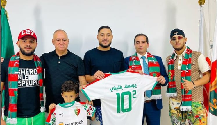 Officiel! Youcef Belaili pose ses valises au Mouloudia d'Alger Youcef Belaili pose avec des supporters et un maillot du Mouloudia d'Alger.