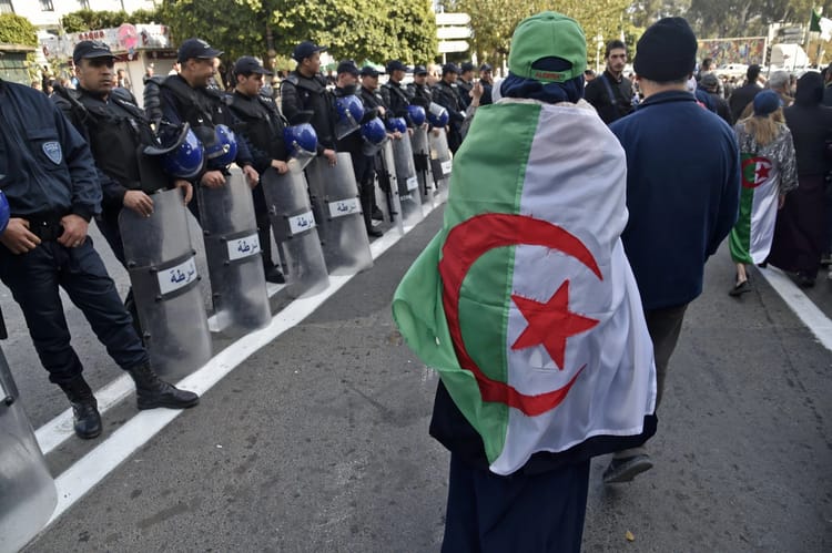 Manifestation avec un homme portant un drapeau algérien.
