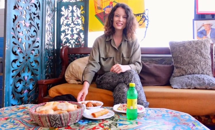 Jeune femme souriante avec snack et boisson dans un salon coloré.