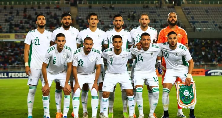 Groupe de joueurs algériens en maillot blanc sur le terrain.