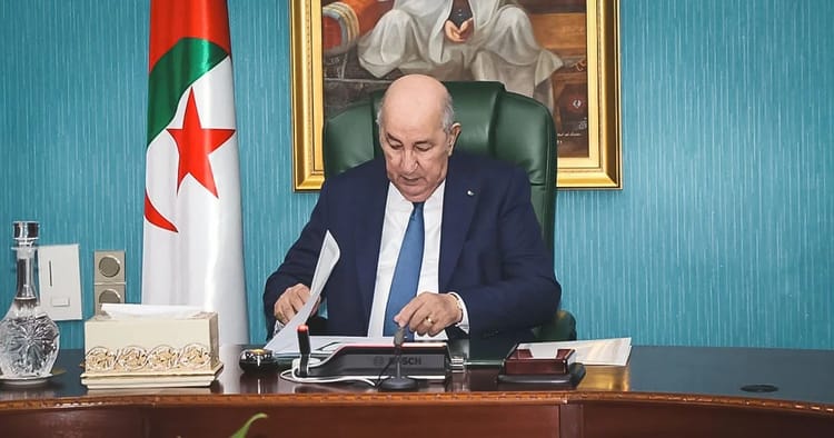 Abdelmadjid Tebboune à son bureau avec drapeau algérien en arrière-plan.